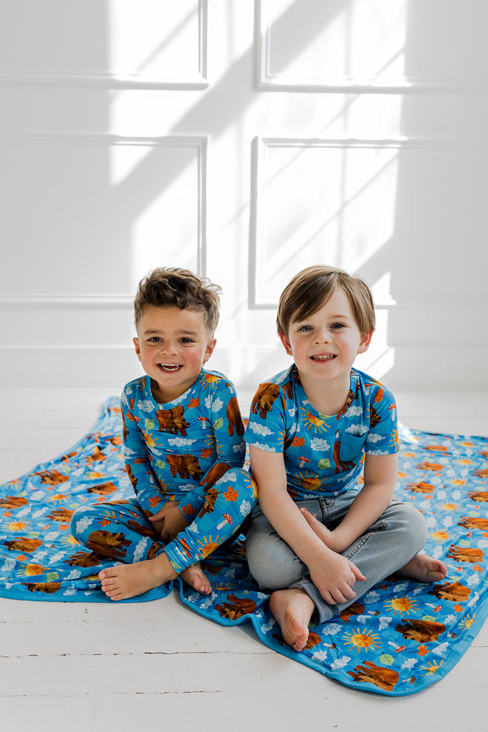 Two children wearing blue short-sleeve tees with brown bear and cloud print, one child also wearing matching pajama pants.