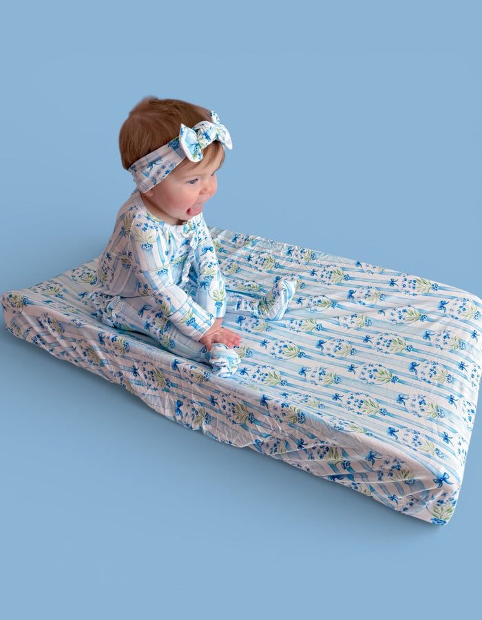 Baby on blue floral changing pad with matching headband and outfit against blue background.