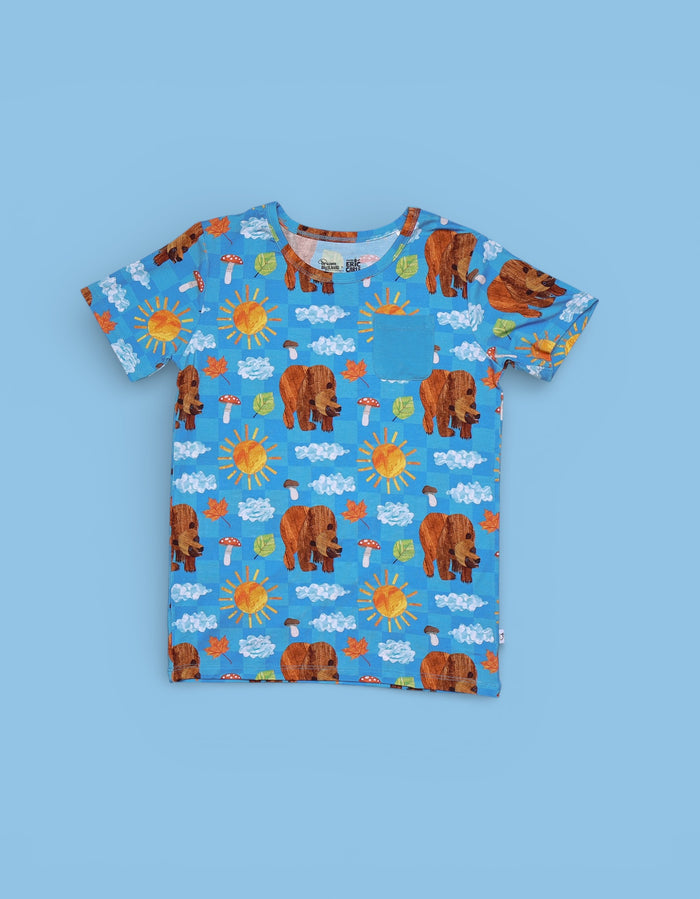 Blue t-shirt with all-over print of brown bears, yellow suns, white clouds, mushrooms, and leaves on blue background.