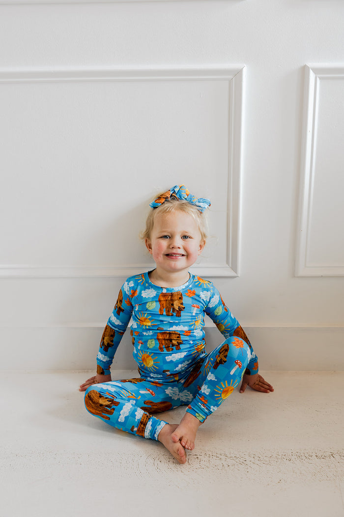 Toddler wearing blue pajama set with bear and sky print, including long-sleeve top, pants, and matching headband.