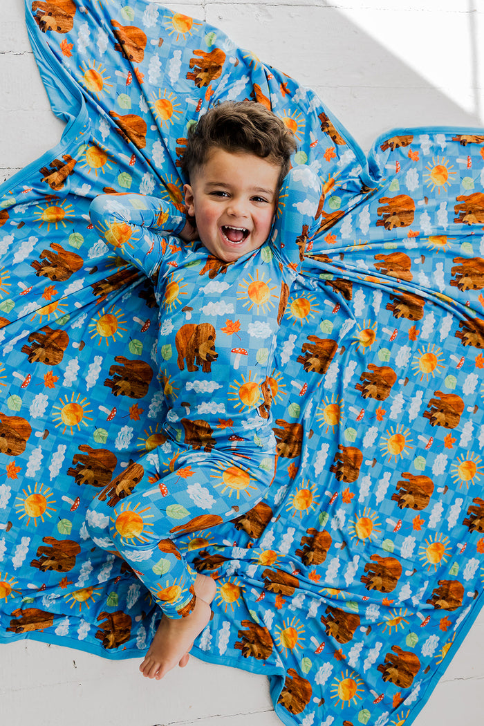 Child wrapped in blue bedding set with bears, suns, clouds, and mushroom print.