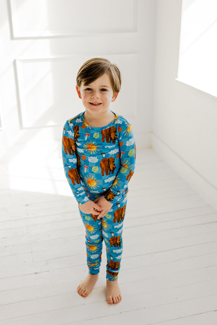 Child wearing blue pajamas with brown bear, sun, and cloud print throughout long-sleeved shirt and matching pants.