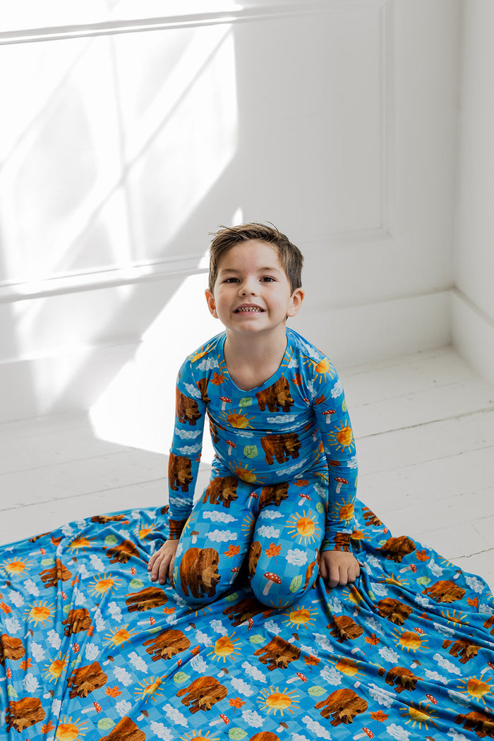 Child wearing blue pajama set with bear, sun, and cloud print throughout shirt and pants.
