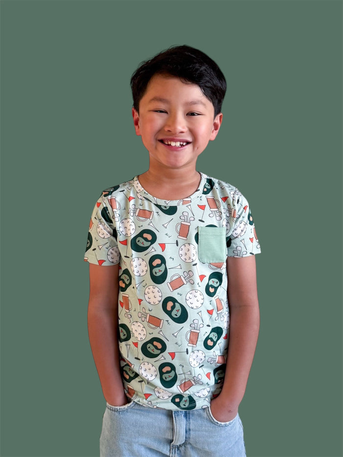 Child's short-sleeve t-shirt with golf-themed print featuring scorecard symbols and golf balls, mint chest pocket, paired wit