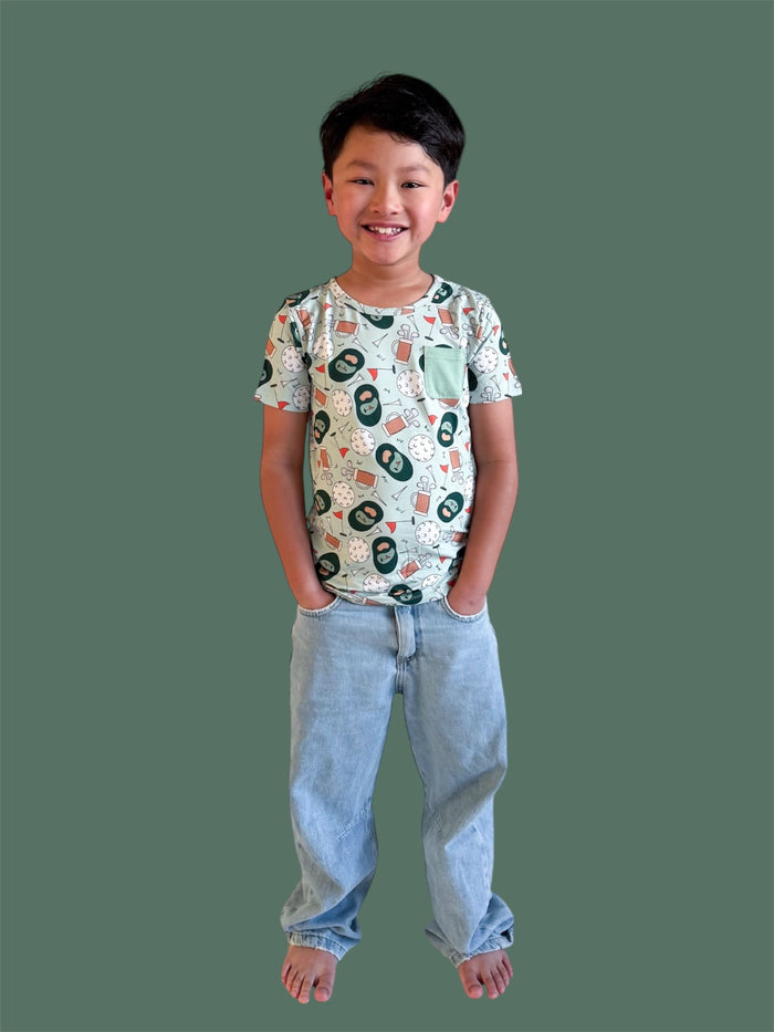 Child wearing short-sleeve tee with golf-themed print including numbers and clubs, mint pocket detail, paired with light blue
