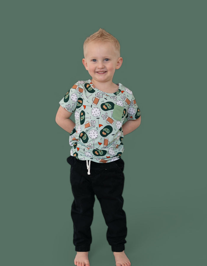 Toddler wearing light gray short-sleeve tee with golf-themed print and black joggers.