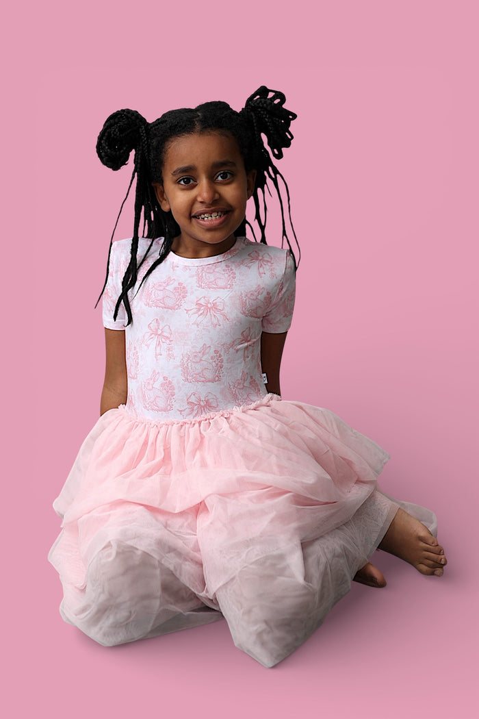 Child wearing white short-sleeve top with pink toile bunny print and layered pink tulle skirt.