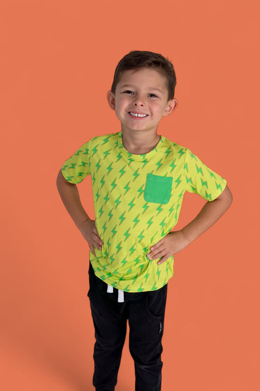 Child wearing yellow short-sleeve tee with green lightning bolt pattern and matching pocket, paired with black pants.
