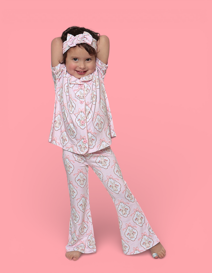 Young girl wearing pink bunny print flare set with matching headband against pink background.