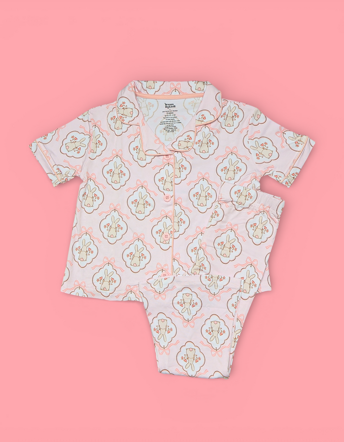 Two-piece children's pajama set with bunny and floral pattern in cream and peach on pink background.