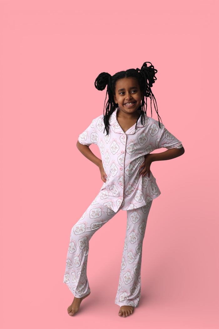 Child wearing white short-sleeve button-up shirt and flared pants with bunny face print throughout.