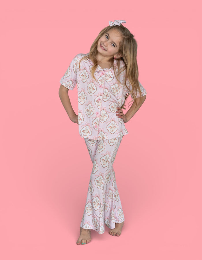 Girl wearing white short-sleeved top and flared pants with bunny and floral print, paired with matching bunny bow headband.