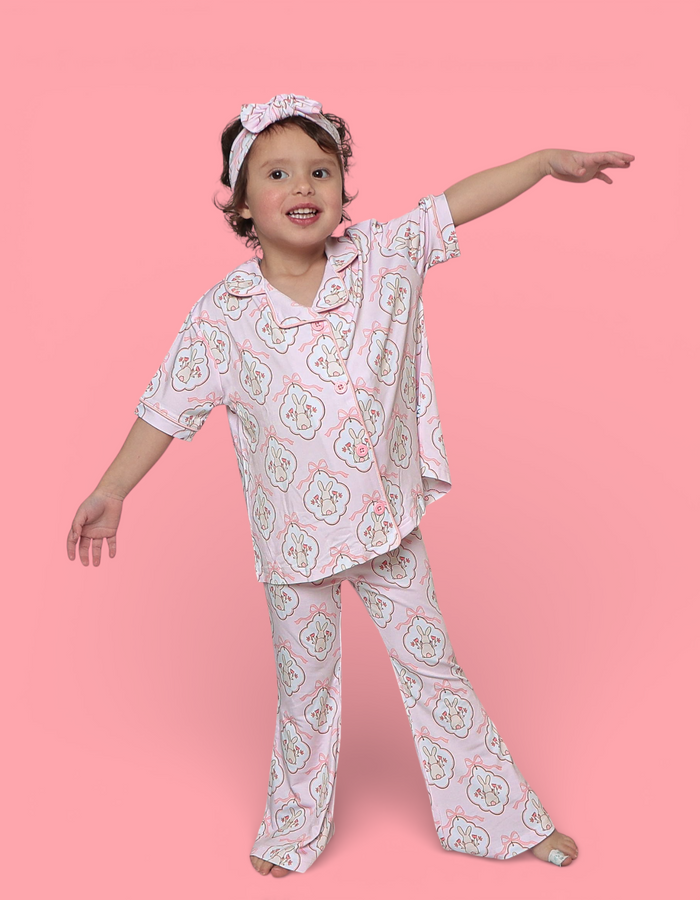 Young child wearing lavender pajama set with bunny print, matching headband, three-quarter sleeve shirt and flared pants.