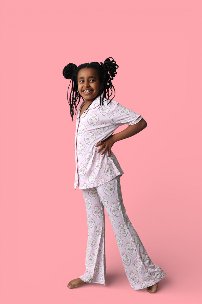 Girl wearing light pink short-sleeve shirt and flared pants with bunny and bow print throughout.