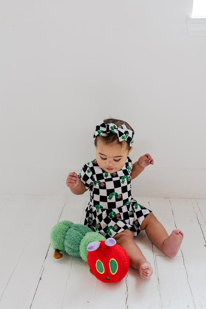 Infant wearing black and white checkered bodysuit dress with green caterpillar print, paired with matching headband.