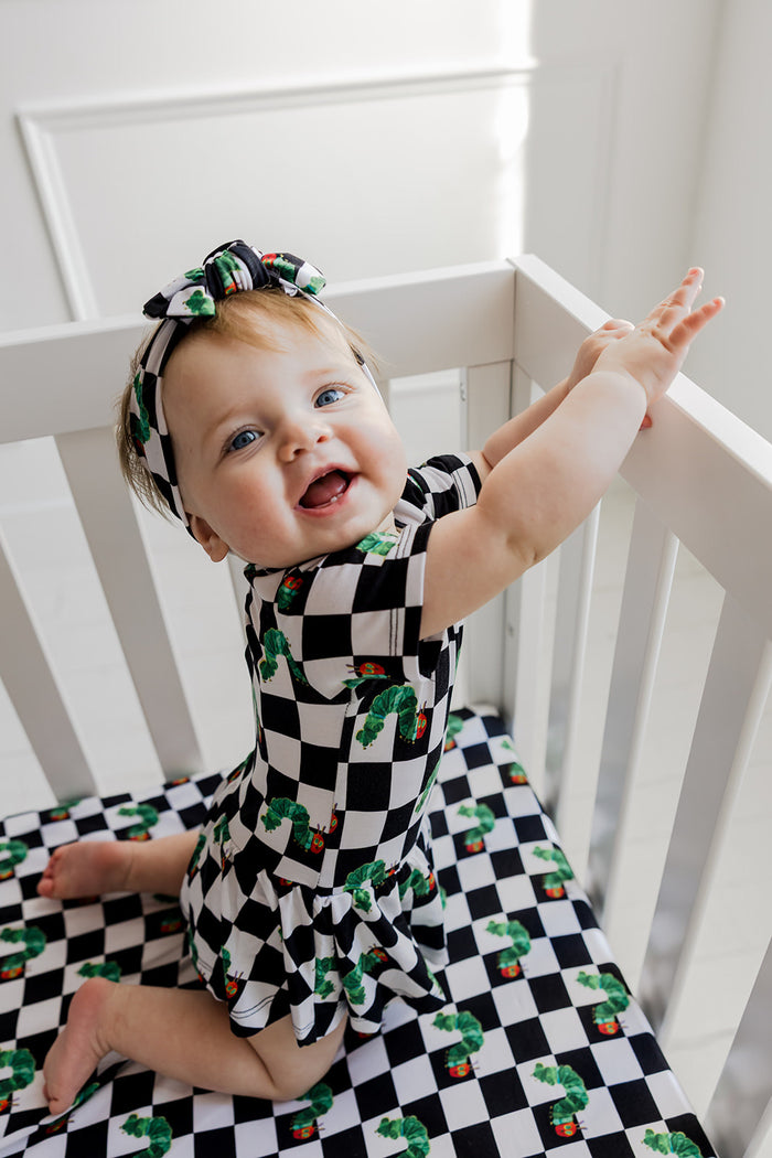 Infant in black and white checkered bodysuit dress with green caterpillar pattern and matching headbow.