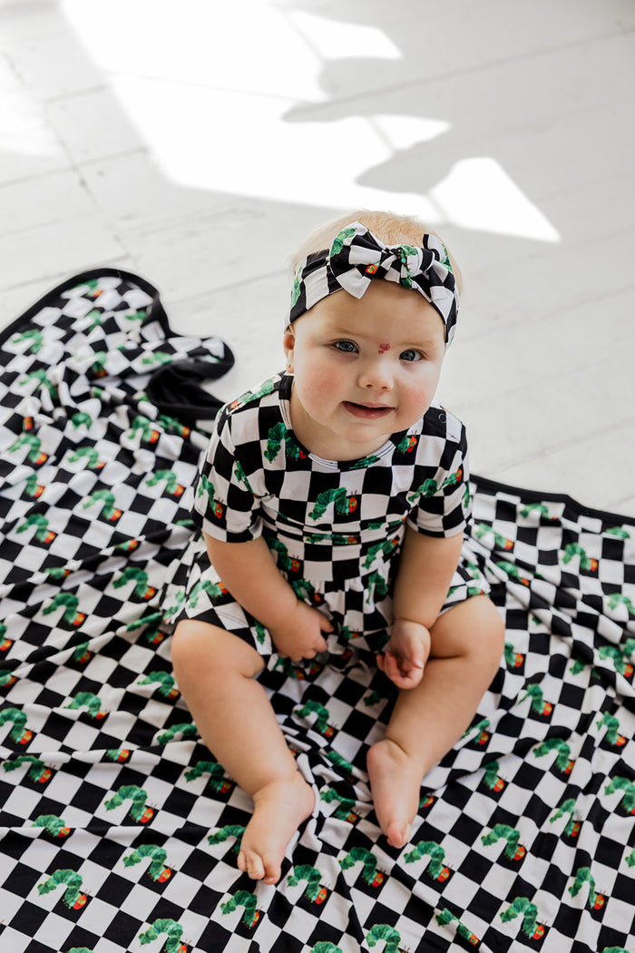 Infant wearing black, white, and green checkered bodysuit dress with matching headband bow.