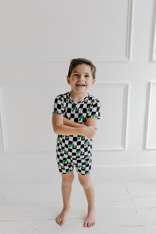 Child wearing black and white checkered short set with green caterpillar print throughout.