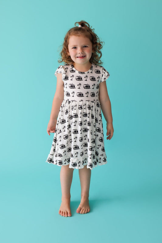 Girl's white dress with black beach-themed print, ruffled cap sleeves, and knee-length fit.