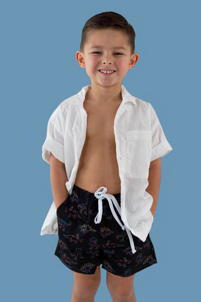 Black swim trunks with colorful dinosaur outlines and white drawstring on child model.