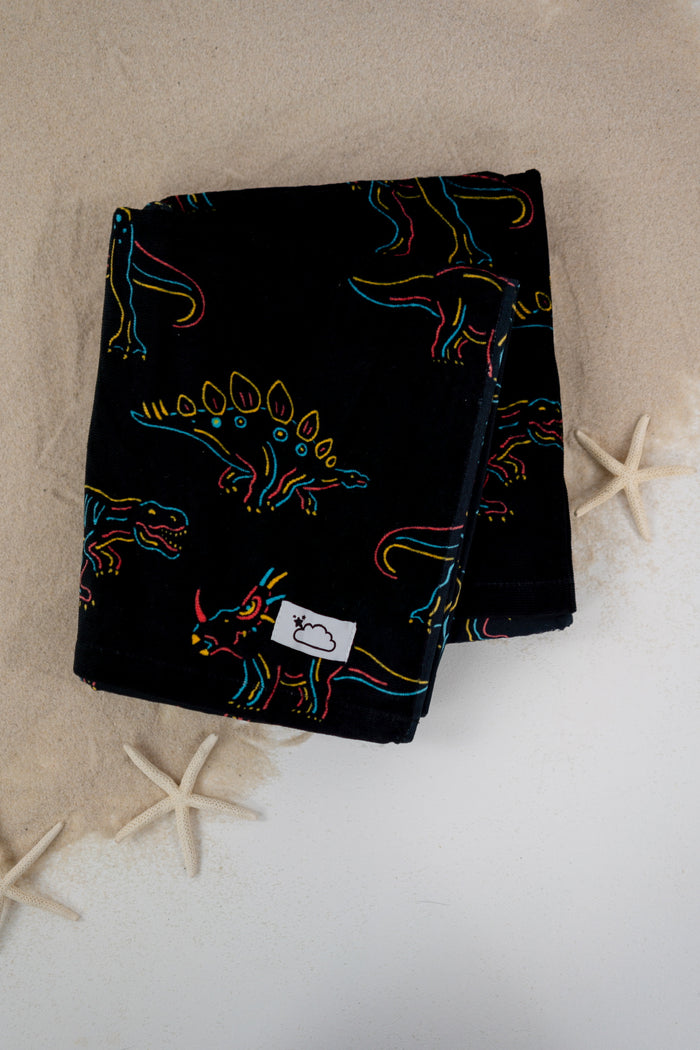 Black towel with colorful neon-outlined dinosaurs in blue, yellow, and red scattered across the fabric.