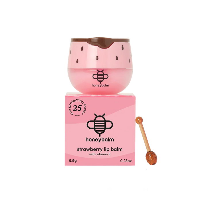 Pink lip balm with strawberry seed design and honeycomb, accompanied by its packaging and a honey stick on a white background.