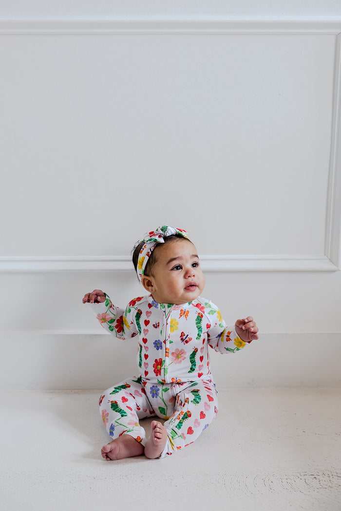 Infant sitting wearing a white romper with multicolored floral and bug print, long sleeves, and matching headband.
