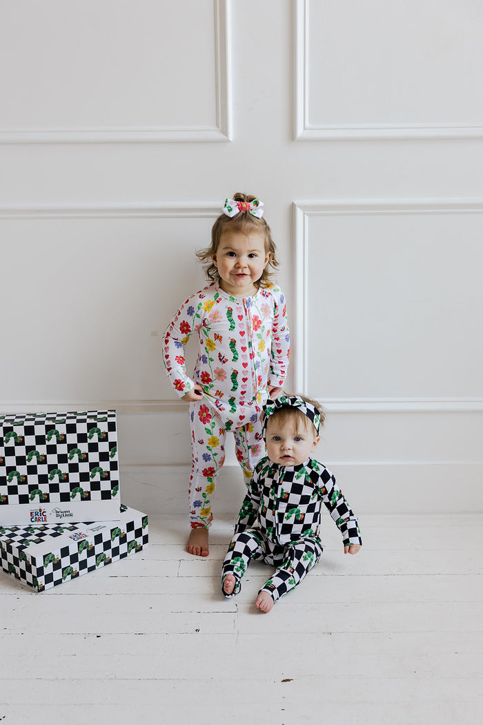 Toddler wearing white long-sleeve romper with colorful floral print and matching hair bow.