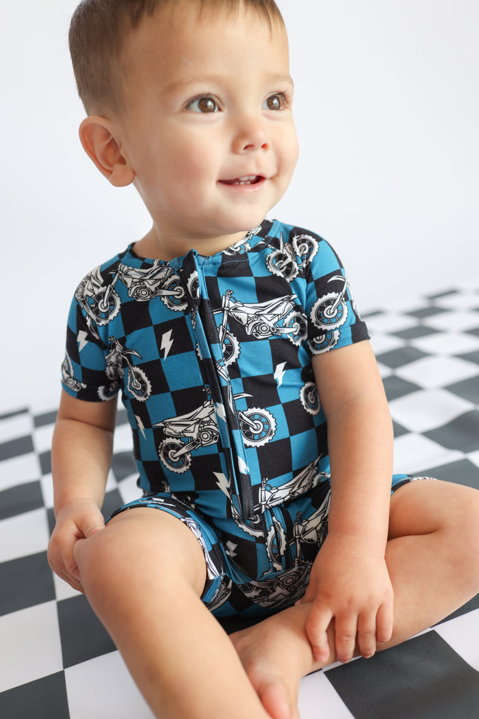 Toddler in blue and black checkered short-sleeve romper with motorcycle print and front zipper.