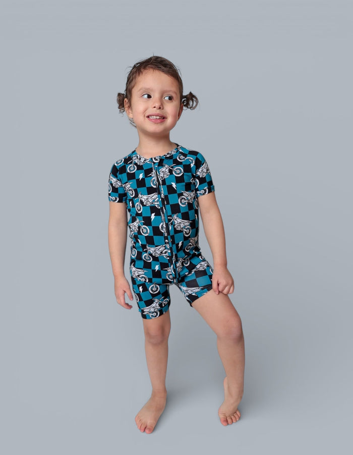Toddler wearing teal and black checkered short-sleeve romper with motorcycle print and front zipper.