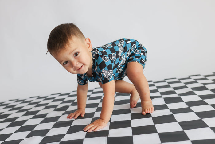 Toddler in blue motorcycle-print short-sleeve romper crawling on checkered floor.