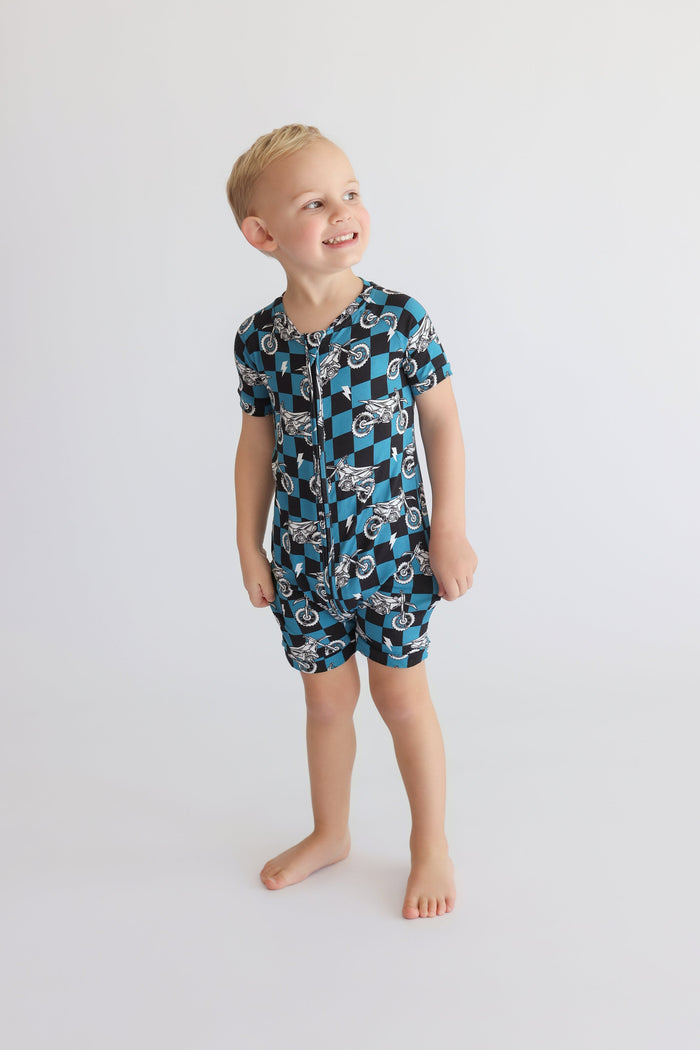 Young child wearing blue and black checkered short-sleeve romper with motorcycle print and front zipper.