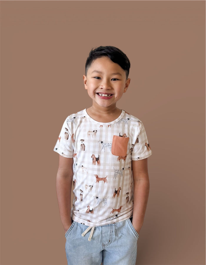 Child's short-sleeve tee in cream with dog print and rust-colored chest pocket, paired with light blue jeans.