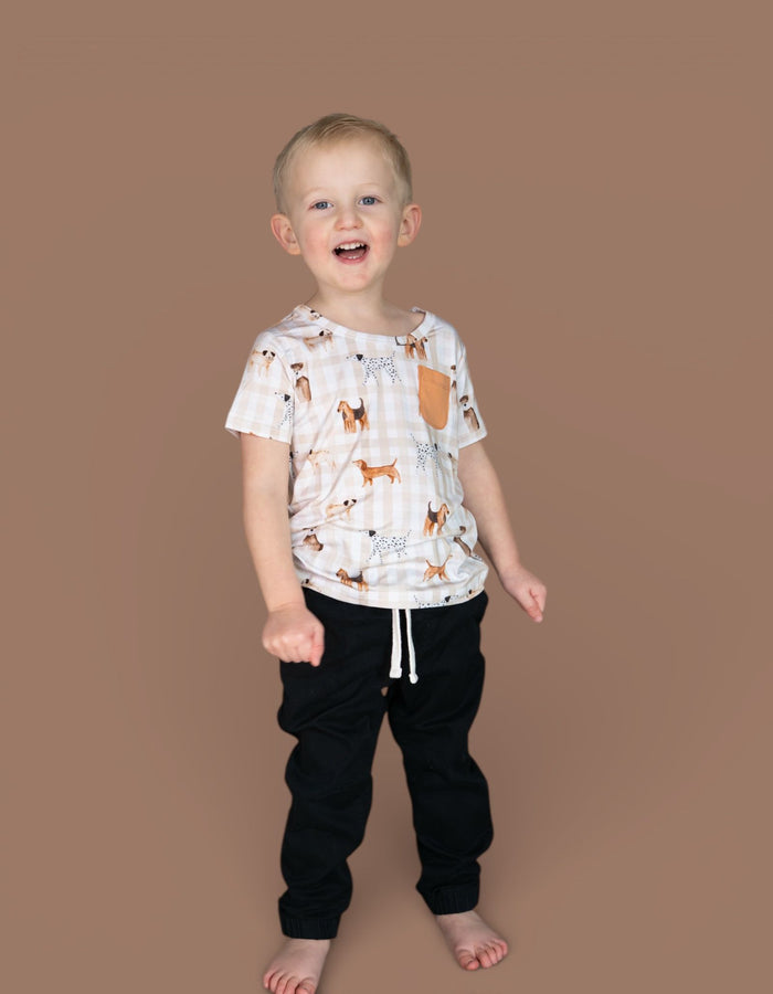 Toddler wearing cream short-sleeve tee with brown and tan dog print and chest pocket, paired with black joggers.