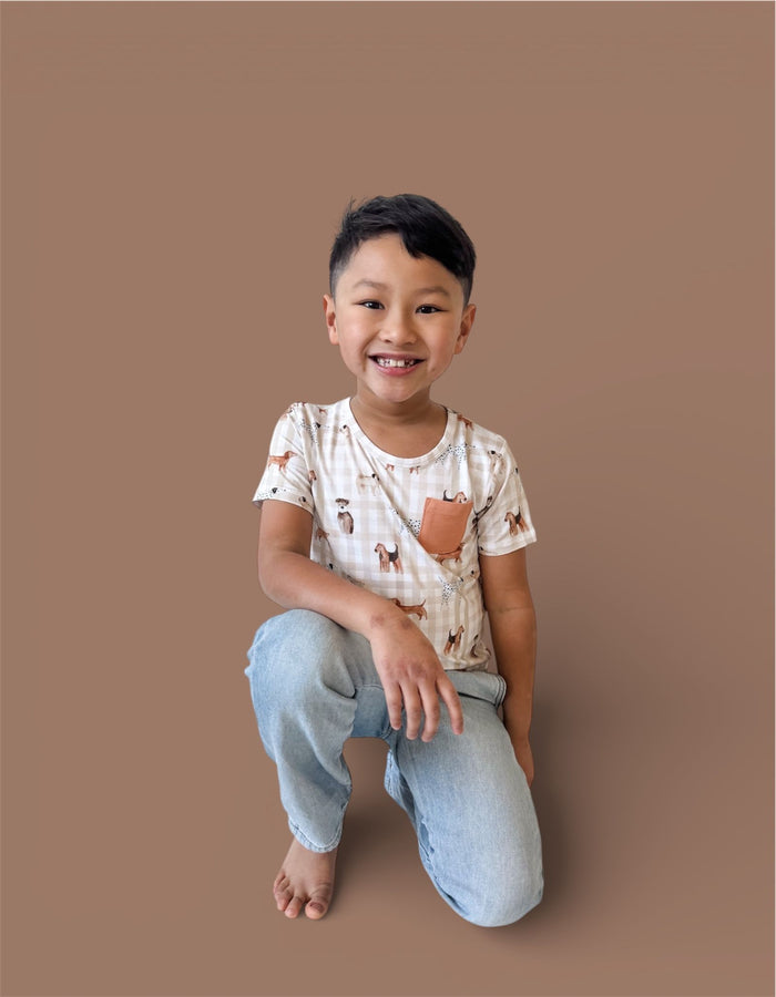 Child wearing cream-colored short-sleeve tee with animal print pattern and orange chest pocket, paired with light blue jeans.