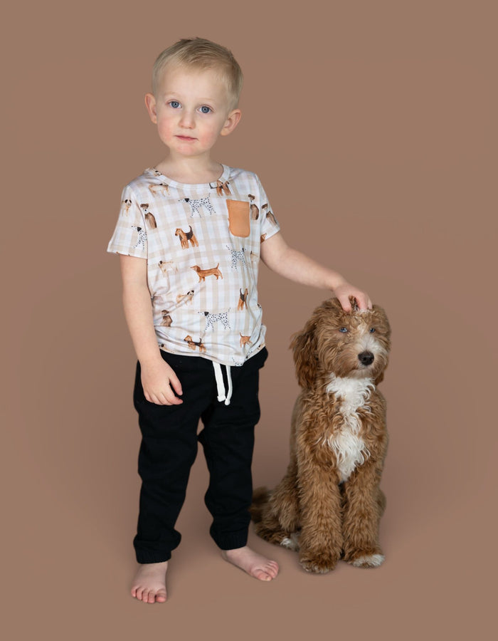 Young child wearing short-sleeved t-shirt with tan and white gingham check pattern and brown dog print, featuring tan chest p