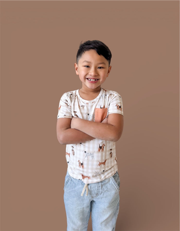 Child wearing cream short-sleeve t-shirt with dog print and orange chest pocket, paired with light blue jeans.