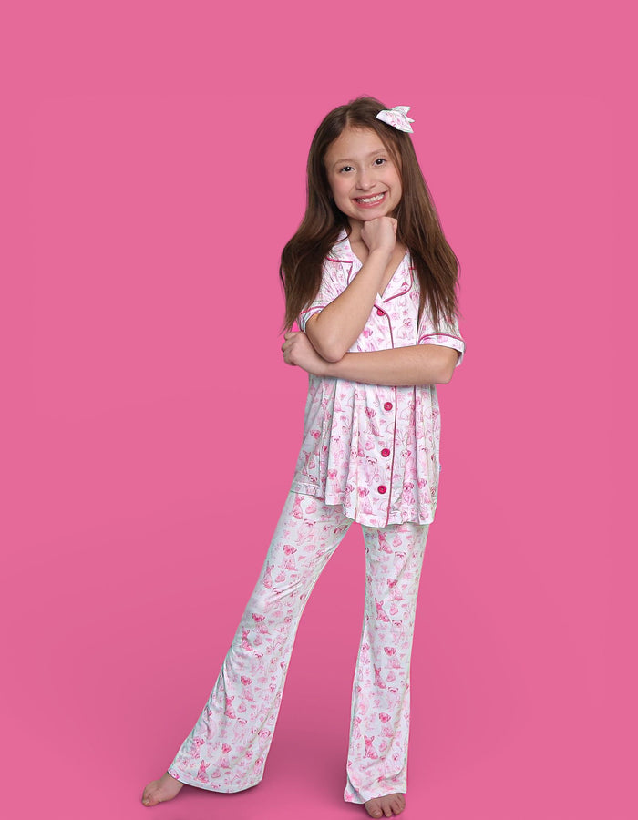 Girl wearing pink and white puppy print short-sleeve shirt with matching flare pants against pink background.