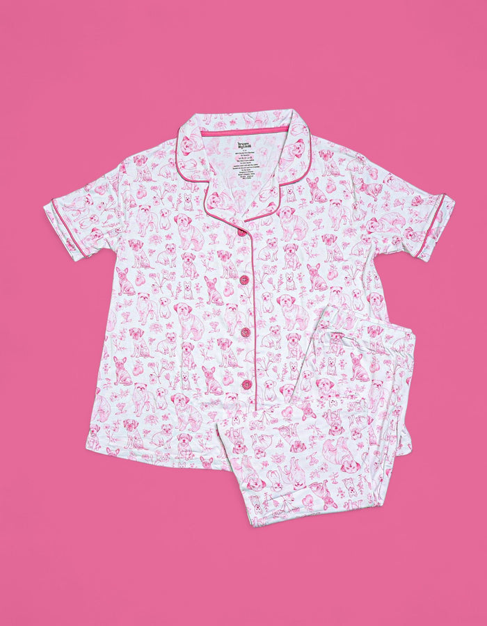 White short-sleeve pajama set with pink puppy toile print, button-front top with collar, and matching flare pants on pink bac