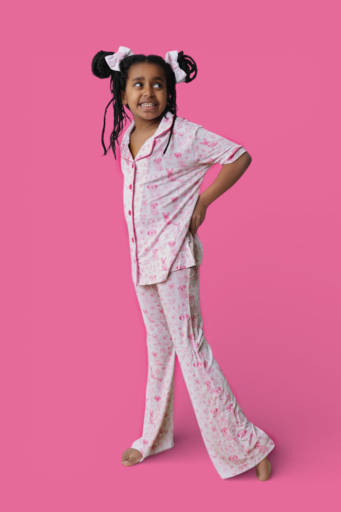 Girl wearing white short-sleeve button-up shirt and flare pants with pink puppy toile pattern.