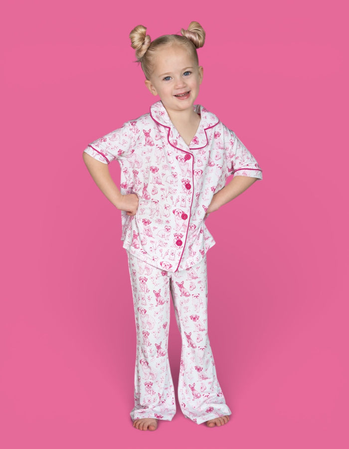 Girl wearing pink and white puppy print pajama set with short-sleeved top and flared pants.