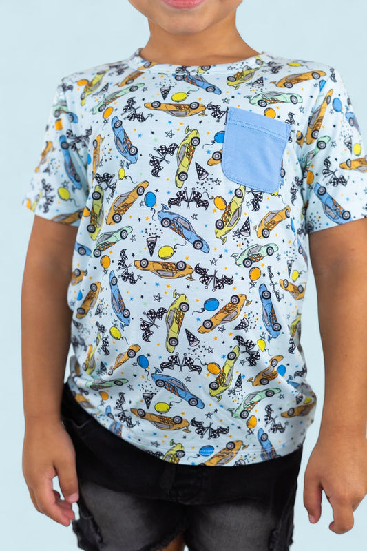Light blue short-sleeve tee with racing cars, balloons, and stars print, featuring a blue chest pocket.