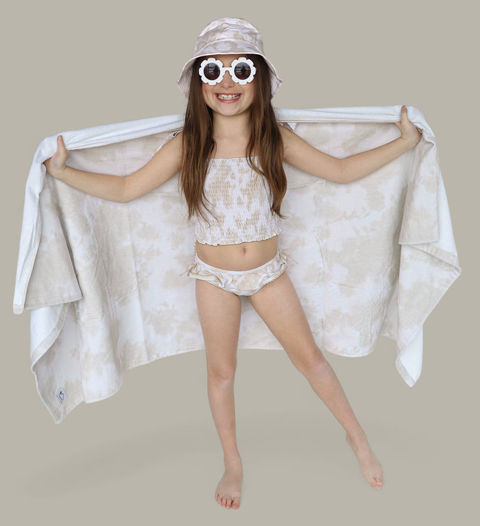 Child wearing light beige towel draped across shoulders with white sunglasses and bucket hat.