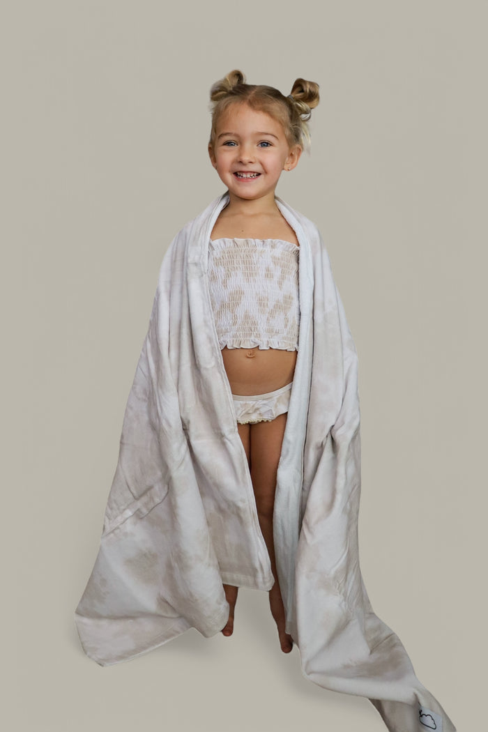 Young child wrapped in a light beige towel worn as a cape over a matching two-piece set.