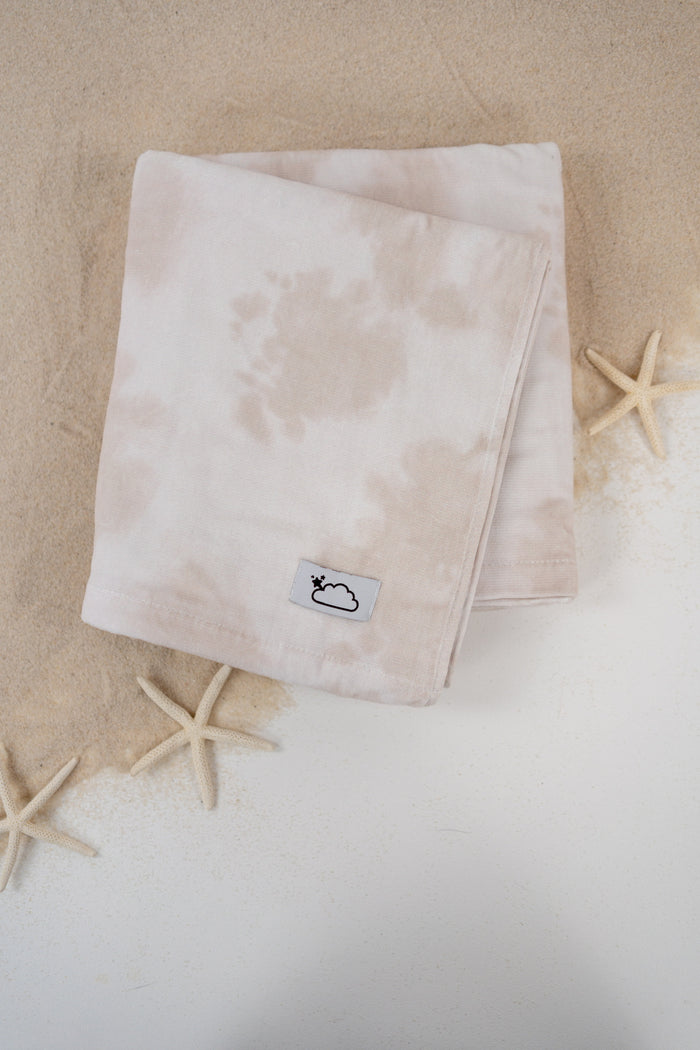 Folded beige towel with small brand label, displayed on sand with starfish beside it.