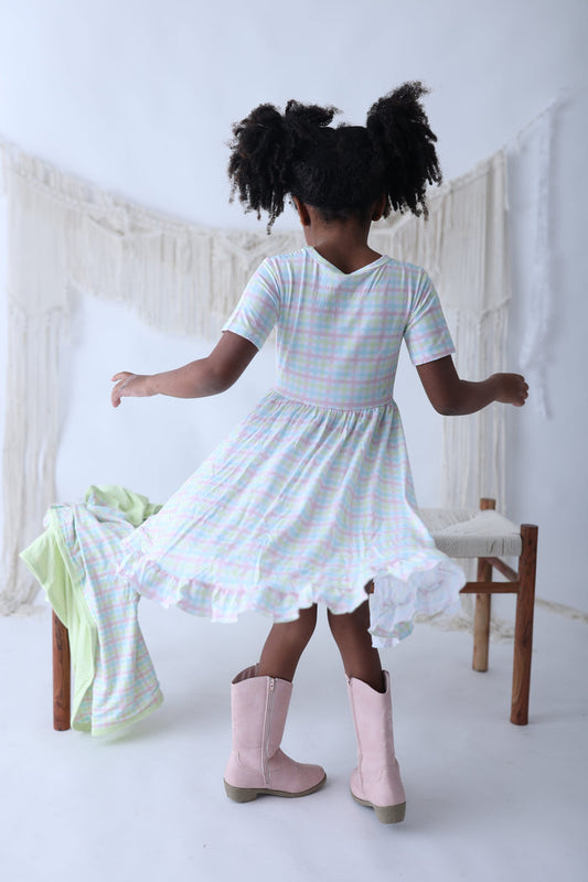 Child wearing pastel gingham short-sleeve dress with ruffled hem and white ruffle trim, paired with pink boots.