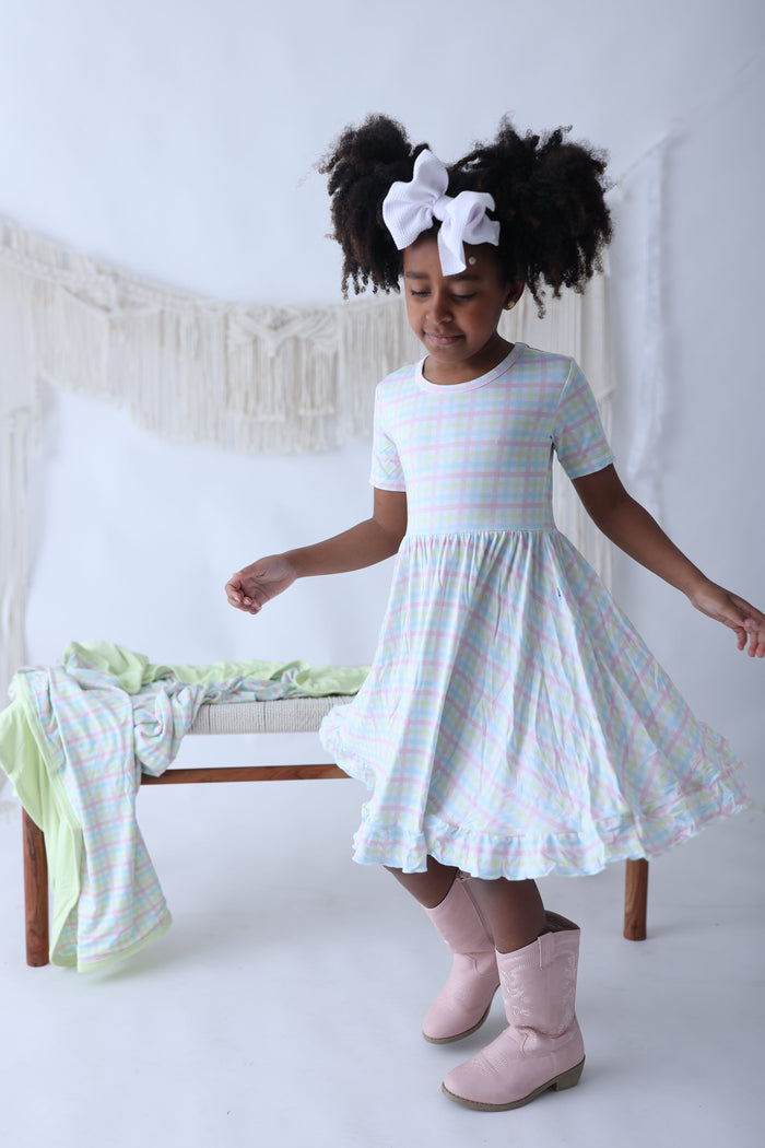 Child's short-sleeve gingham dress in pastel pink, blue, and green with gathered skirt and ruffled hem.