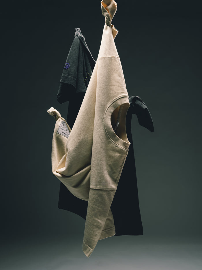 Beige und schwarze Kleidungsstücke kunstvoll an den Ärmeln aufgehängt und frei vor einem dunkelgrauen Hintergrund schwebend.