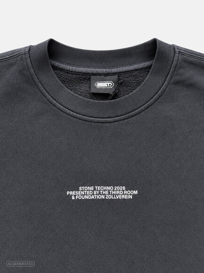 Nahaufnahme des dunkelgrauen Sweatshirts mit kleinem weißen Brustprint „STONE TECHNO 2026 PRESENTED BY THE THIRD ROOM & FOUNDATION ZOLLVEREIN“. Sichtbar sind außerdem der gerippte Rundhalskragen und das schwarze Nackenlabel mit Stone-Techno-Logo.